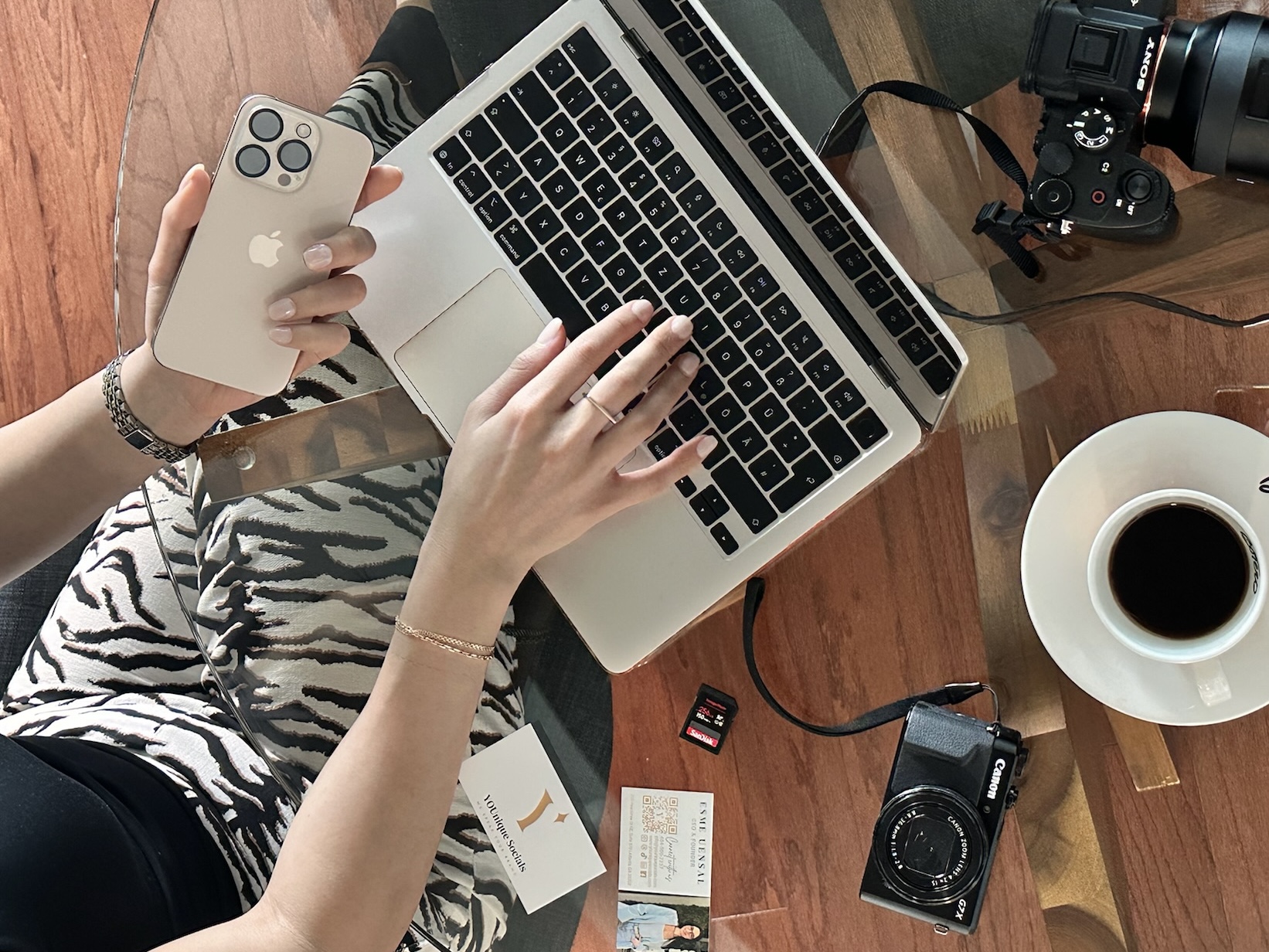Employee at YOUnique Socials working on a laptop with their phone in the left hand and a cup of coffee